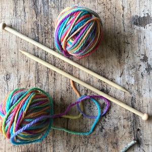 Peut inclure: Deux pelotes de laine colorée à rayures arc-en-ciel et deux aiguilles à tricoter en bois.
