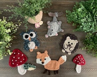 Puede incluir: Un conjunto de cinco peluches de animales del bosque de crochet y dos setas rojas y blancas de crochet. Los animales incluyen un zorro, un búho, un erizo, una ardilla y un mapache.