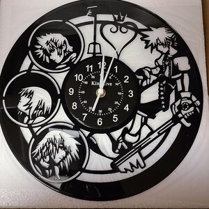 May include: Black vinyl record clock featuring a white silhouette of characters from the Kingdom Hearts video game series. The clock face has black numbers and a white background. The clock hands are black.