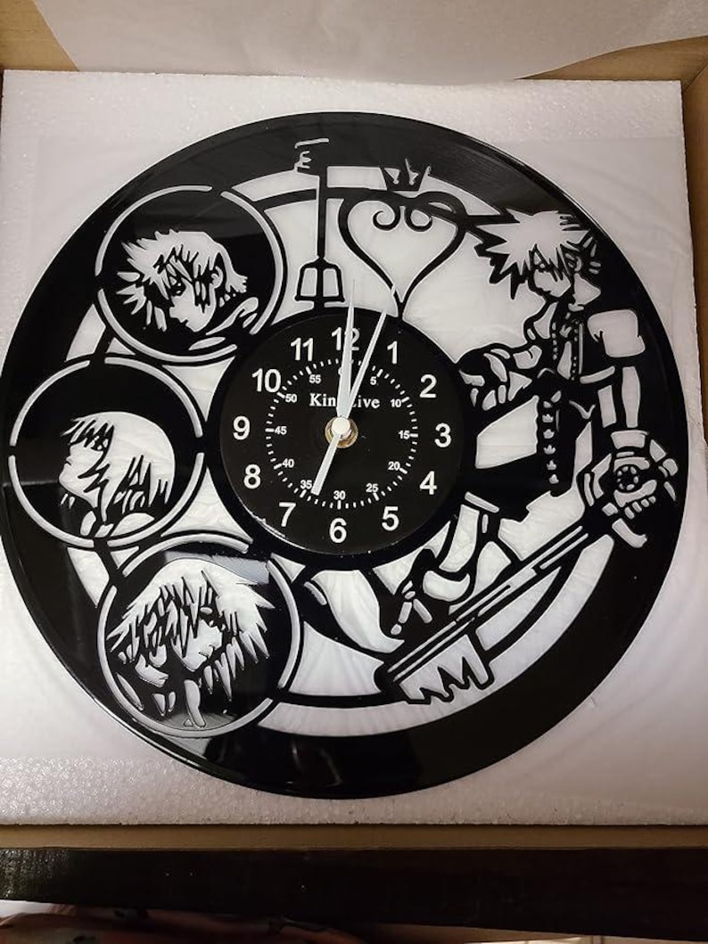 May include: Black vinyl record clock featuring a white silhouette of characters from the Kingdom Hearts video game series. The clock face has black numbers and a white background. The clock hands are black.