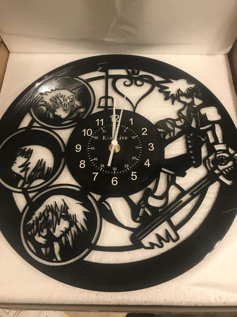 May include: Black vinyl record clock featuring a silhouette of a character from the Kingdom Hearts video game series. The clock face is white with black numbers and a black hand. The clock is in a box.