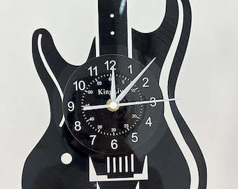 Könnte beinhalten: Schwarze Schallplattenuhr in Form einer E-Gitarre. Das Zifferblatt hat weiße Zahlen und Zeiger. Das Zifferblatt hat auch den Text "King Liv" aufgedruckt.