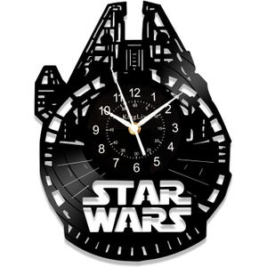 Peut inclure: Une horloge en vinyle noir représentant une silhouette du Faucon Millenium de Star Wars. Le cadran de l'horloge est blanc avec des chiffres et des aiguilles noirs. Les mots "STAR WARS" sont imprimés en blanc sous le cadran de l'horloge.