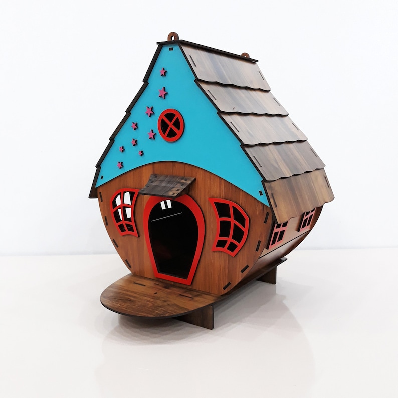 May include: A wooden house shaped like a birdhouse with a blue roof and red accents. The house has a small porch and a window with a red frame. The roof has a wood grain pattern and is decorated with pink stars.