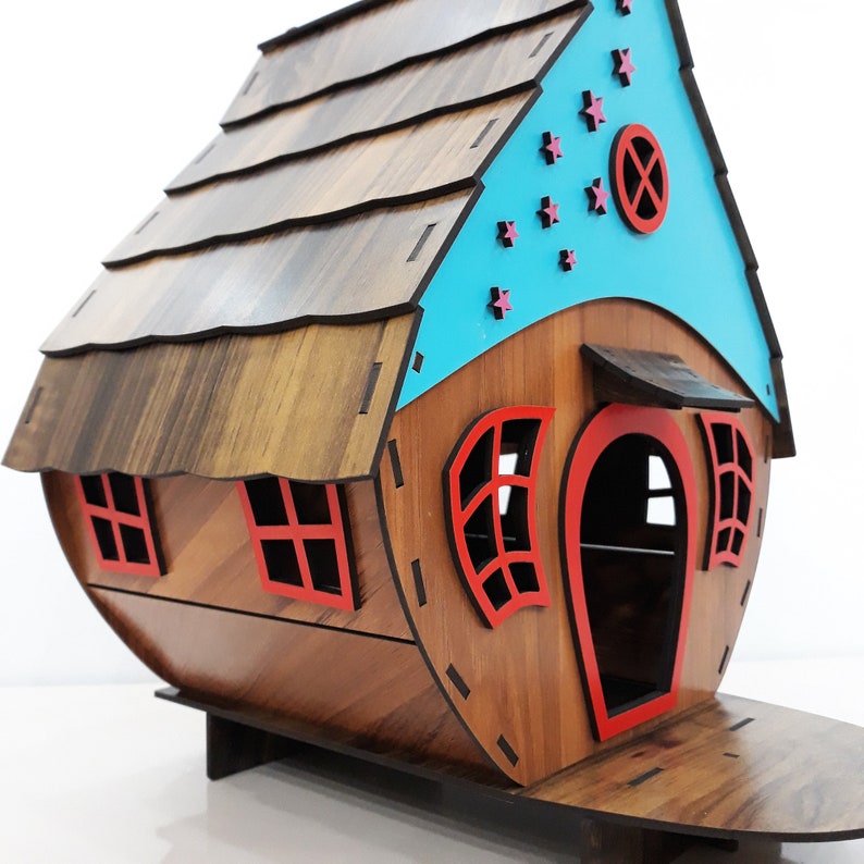 May include: A wooden toy house with a blue roof and red trim. The roof has a brown wood grain pattern and the house has a small door and windows. There are pink stars on the blue roof.