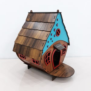 May include: A wooden birdhouse with a blue roof and red accents. The birdhouse has a small porch and a window. The birdhouse is made of wood and has a rustic look.