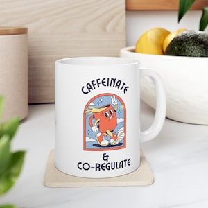 Op de afbeelding: Witte keramische mok met een cartoonillustratie van een koffiekopje met een gezicht en armen die loopt. De tekst "CAFFEINE & CO-REGULATE" staat op de mok gedrukt.