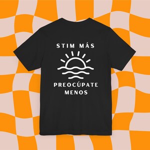 May include: Black t-shirt with white text that reads "Stim Más Preocúpate Menos" and a graphic of a sun setting over the ocean.