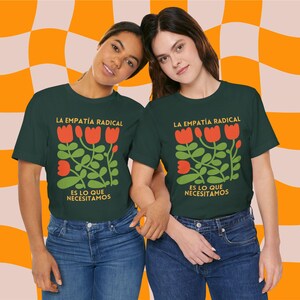 May include: Two people wearing dark green t-shirts with a graphic of red flowers and green leaves. The text on the shirts reads "La Empatía Radical" and "Es lo que necesitamos".