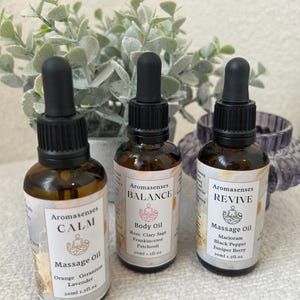 May include: Three Aromasenses massage oil bottles with black droppers. The labels read "CALM", "BALANCE", and "REVIVE". The "CALM" bottle lists orange, geranium, and lavender. The "BALANCE" bottle lists rose, clary sage, frankincense, and patchouli. The "REVIVE" bottle lists marjoram, black pepper, and juniper berry.