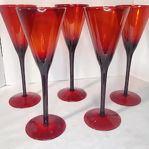 May include: A set of five tall, slender drinking glasses featuring a vibrant red bowl that transitions into a deep, dark red stem and a circular base. Each glass has a wide, flared rim and a smooth, polished finish, standing upright.