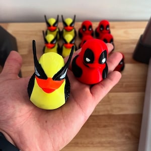 May include: A collection of novelty duck figurines. One yellow duck with black accents and a red beak, and several red ducks with black accents. The ducks are arranged on a wooden surface.