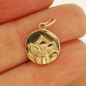 May include: A gold-toned charm featuring a detailed lotus flower design. The charm is round and has a smooth, polished finish.
