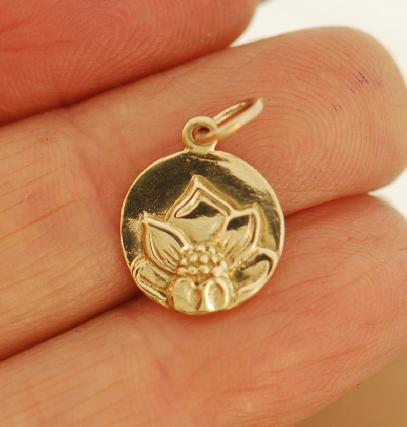 May include: A gold-toned charm featuring a detailed lotus flower design. The charm is round and has a smooth, polished finish.