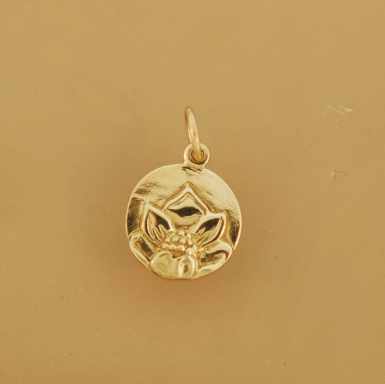 May include: A gold-colored pendant charm featuring a detailed lotus flower design. The charm is round and has a smooth, polished finish.