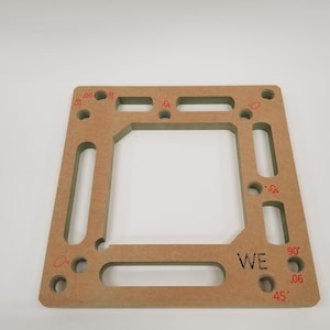May include: A light brown wooden jig with cutouts for different angles, marked with red numbers and degrees. The jig is labelled "WE" and has markings for 0, 45, and 90 degrees.