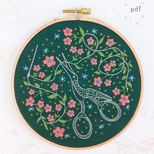 May include: A green embroidery hoop featuring a white outline of a bird and scissors, surrounded by pink flowers and white stars. The text "pdf" is in the top right corner of the image. The text "COZYBLUE handmade" is at the bottom of the image.