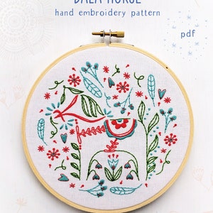 May include: Embroidered hoop art featuring a red and green Dala horse surrounded by flowers and leaves. The hoop is on a white background with the text "DALA HORSE hand embroidery pattern pdf COZYBLUE handmade".