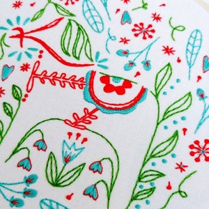 May include: Embroidered design featuring a variety of flowers and leaves in shades of red, green, and blue. The design is stitched on a white fabric background.