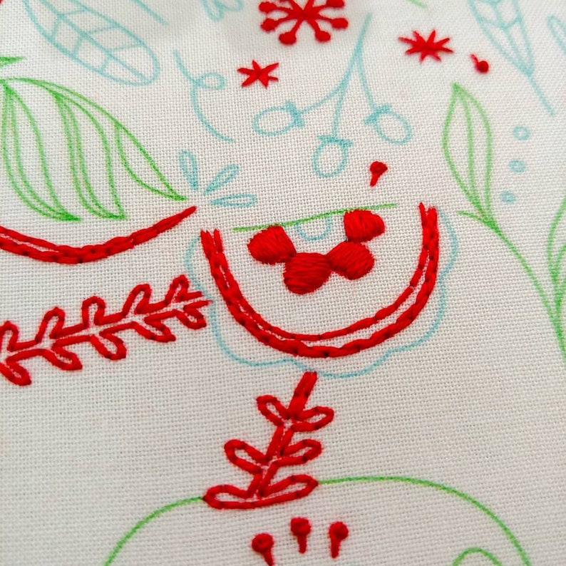 May include: Red embroidery on white fabric with a floral design. The embroidery includes leaves, flowers, and a small red berry cluster.