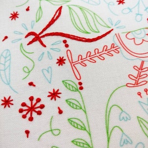 May include: A white fabric background with red and green embroidery. The embroidery features a variety of designs, including flowers, leaves, and hearts.