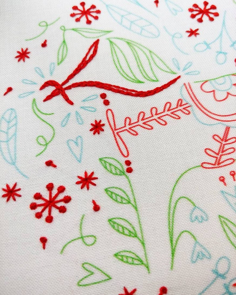 May include: A white fabric background with red and green embroidery. The embroidery features a variety of designs, including flowers, leaves, and hearts.