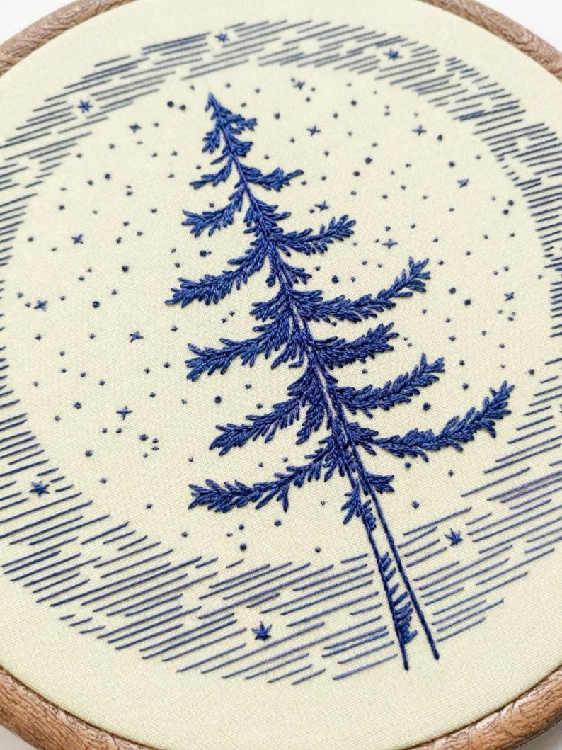Może przedstawiać: Haftowany obręcz z niebieskim drzewem sosnowym na tle nocnego nieba.