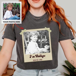 May include: Dark gray t-shirt featuring a black and white photo print. The photo is of a young child and is labeled "I'm Vintage SINCE 1986". A smaller photo is shown in the upper left corner with the text "YOUR PHOTO HERE".