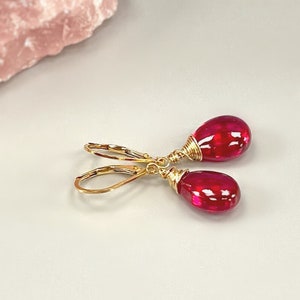 May include: A pair of gold dangle earrings with red teardrop-shaped gemstones.
