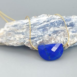 May include: A gold chain necklace with a large, faceted, blue lapis lazuli pendant. The pendant is shaped like a half-circle.