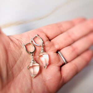 May include: A pair of silver earrings with clear quartz teardrop-shaped stones. The stones are wrapped in silver wire and hang from silver hoops.
