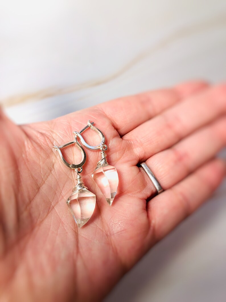 May include: A pair of silver earrings with clear quartz teardrop-shaped stones. The stones are wrapped in silver wire and hang from silver hoops.