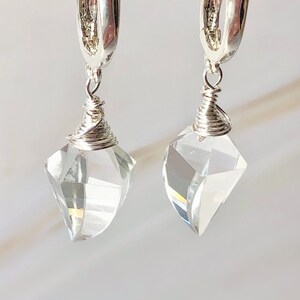 May include: A pair of silver hoop earrings with clear crystal teardrop pendants. The earrings are made with wire wrapped around the crystal.