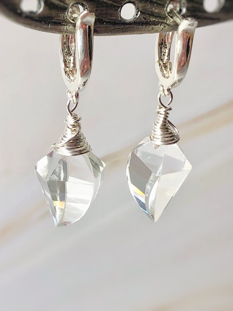 May include: A pair of silver hoop earrings with clear crystal teardrop pendants. The earrings are made with wire wrapped around the crystal.