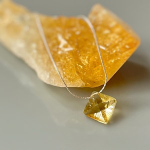 May include: A delicate silver chain necklace with a square-shaped, faceted, yellow citrine gemstone pendant.