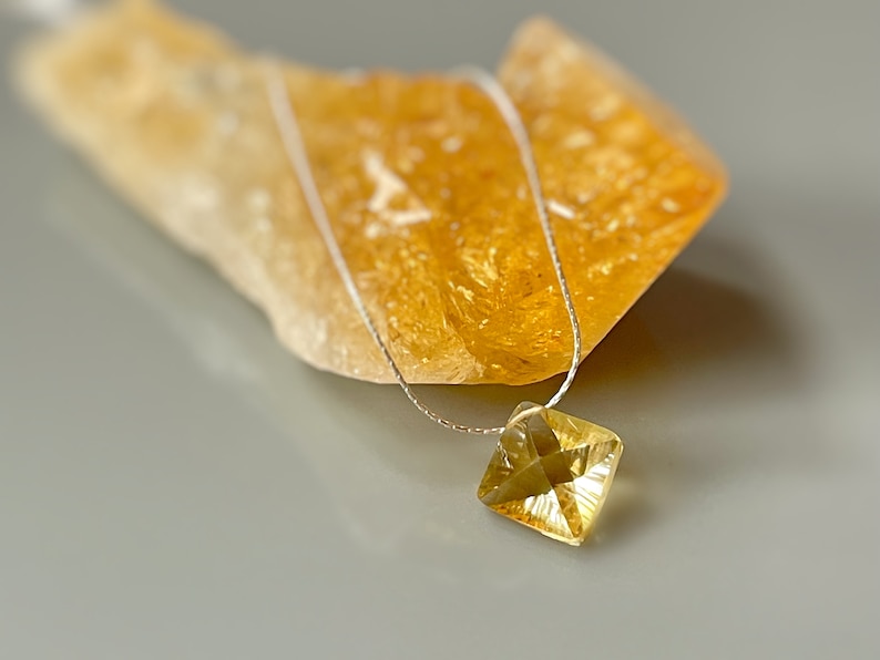 May include: A delicate silver chain necklace with a square-shaped, faceted, yellow citrine gemstone pendant.
