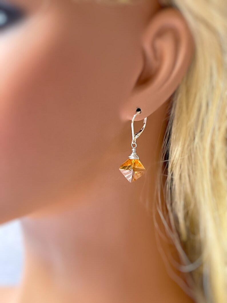 May include: A pair of silver dangle earrings with a clear, faceted, amber-colored crystal pendant.