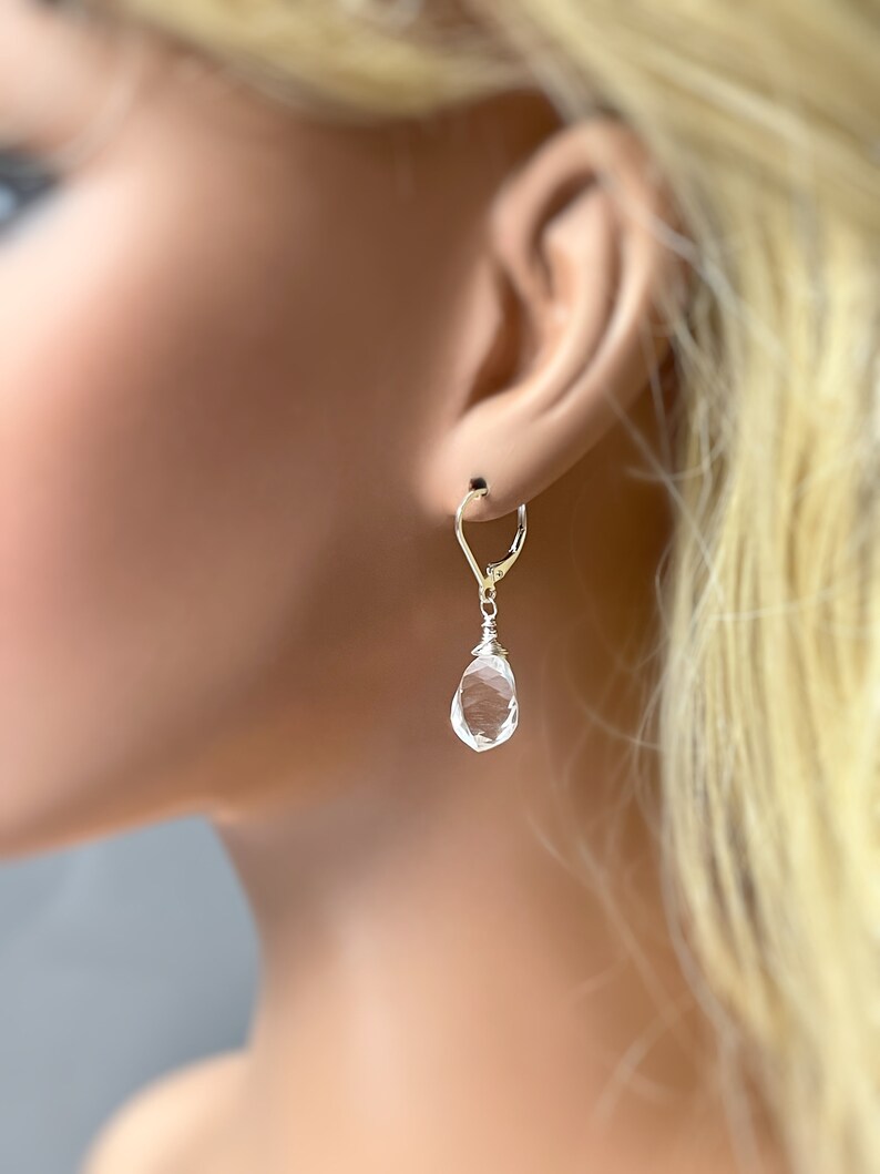 May include: Silver dangle earrings with a clear teardrop-shaped crystal.