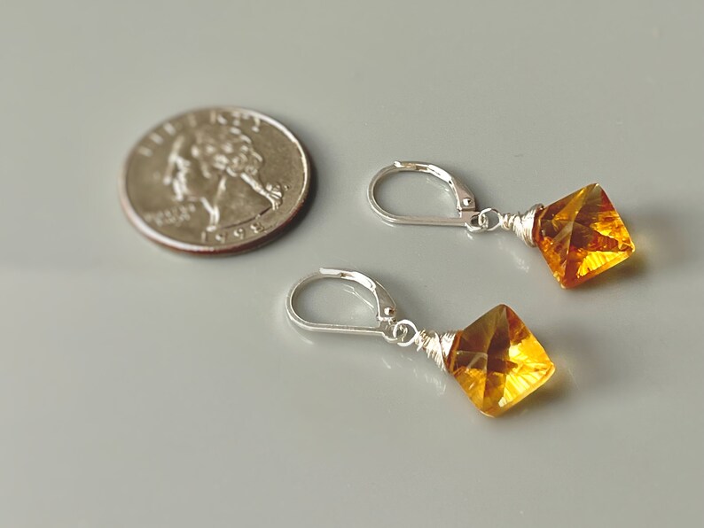May include: A pair of silver earrings with amber-colored gemstone drops. The earrings are approximately the size of a US quarter.