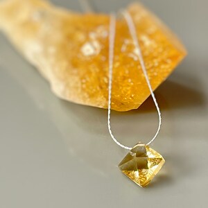 May include: A delicate gold necklace with a faceted, square-shaped pendant. The pendant is a light yellow color and has a subtle sparkle.