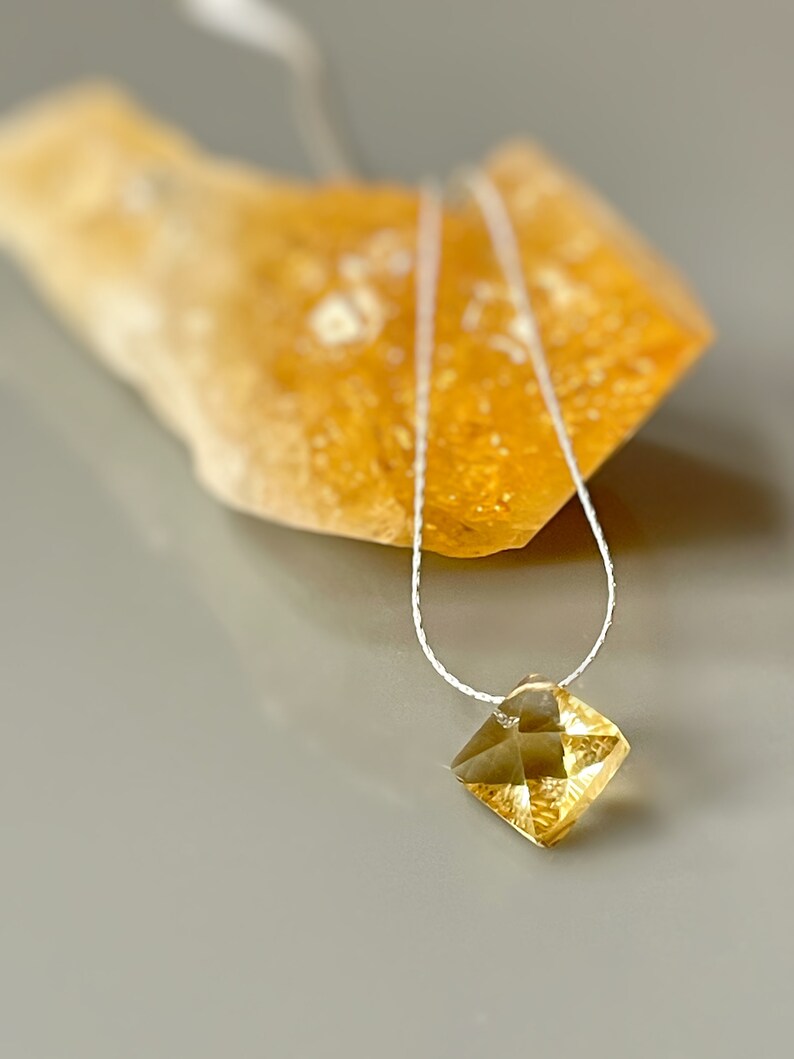 May include: A delicate gold necklace with a faceted, square-shaped pendant. The pendant is a light yellow color and has a subtle sparkle.