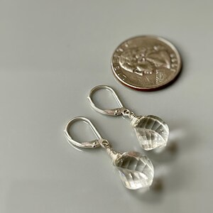 May include: A pair of silver earrings with clear crystal teardrop-shaped stones. The earrings are approximately the size of a US quarter.