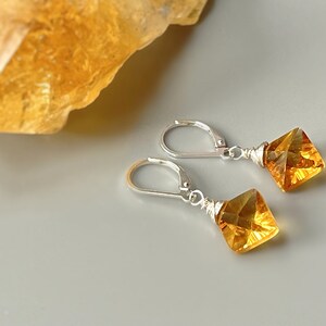 May include: A pair of silver earrings with a square-shaped amber gemstone dangling from each earring.