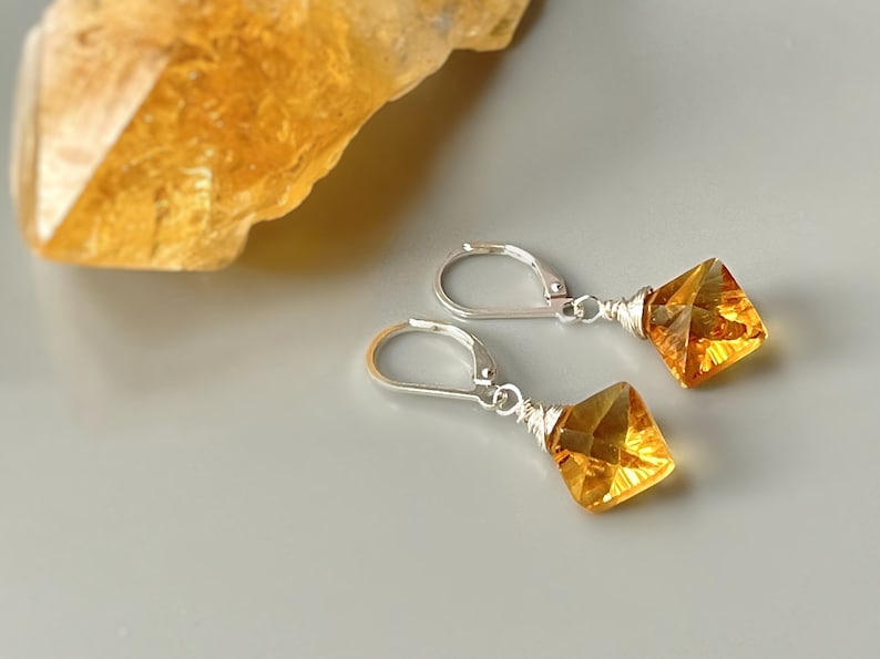 May include: A pair of silver earrings with a square-shaped amber gemstone dangling from each earring.