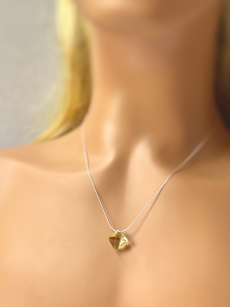 May include: A delicate silver chain necklace with a small, square-shaped, yellow gemstone pendant.