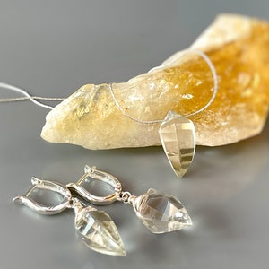 May include: A silver necklace and earrings set with clear quartz crystal pendants. The necklace is on a clear cord and the earrings have silver hoops.