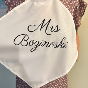 Puede incluir: Cuadrado de tela blanca con el texto "Mrs Bozinoski" bordado en letra cursiva negra.
