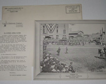 May include: A black and white photograph of a large crowd gathered for the funeral of President William McKinley in Canton, Ohio on September 1901. The photo shows the procession moving through the streets, with a large crowd of mourners lining the sidewalks.