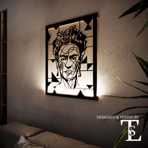 Può includere: Ritratto in bianco e nero di Frida Kahlo in linea d'arte, in una cornice quadrata con una luce dietro. La cornice è su una parete bianca. Il testo "DESIGNED & TESTED BY TS" è sotto la cornice.