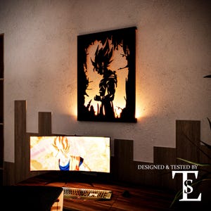 Pode incluir: Uma peça de arte de parede preta com a silhueta de um personagem com cabelo espetado, contra um fundo laranja brilhante. A obra de arte é montada numa parede de cor clara. Um monitor de computador e um teclado são visíveis abaixo.